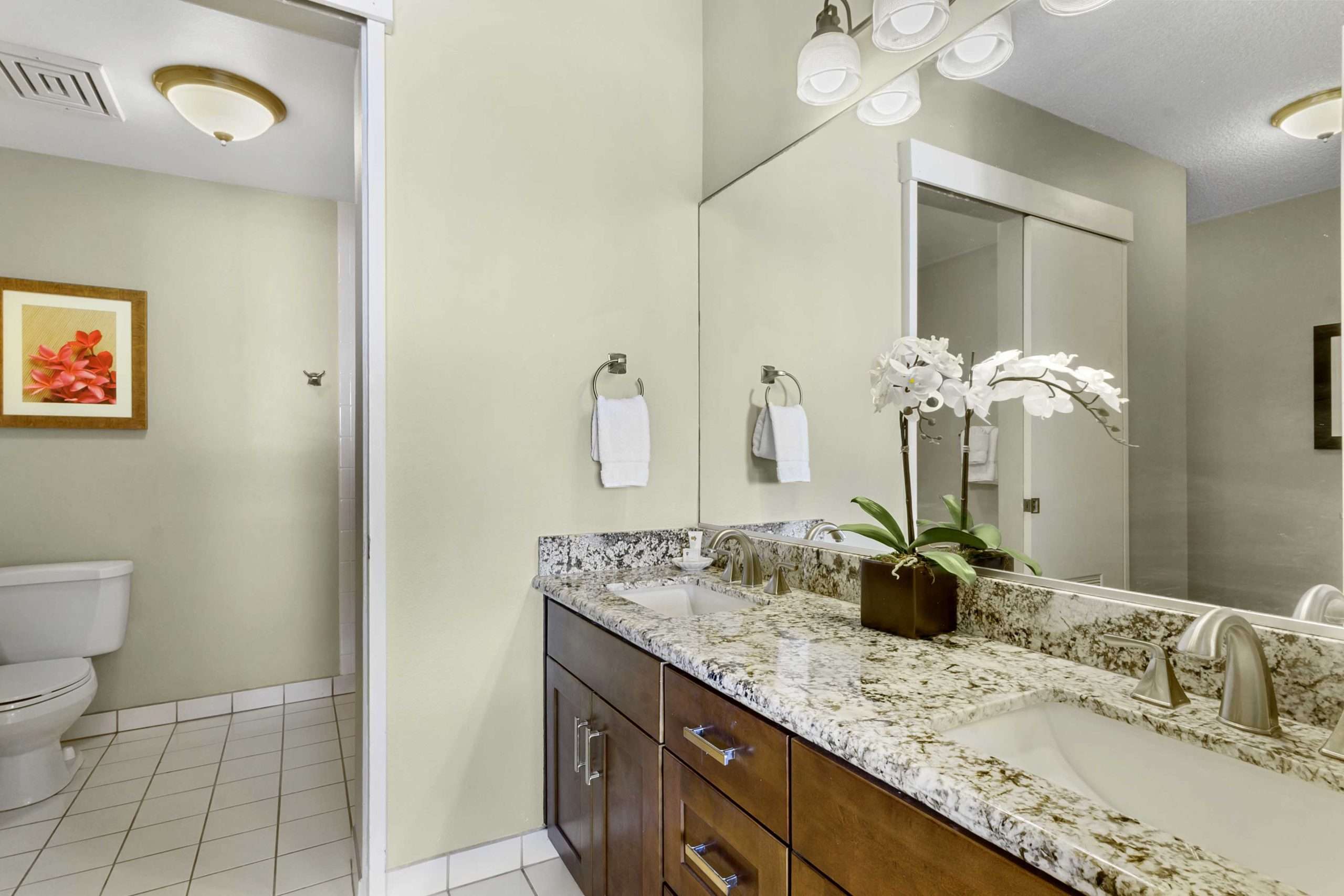 Two-bedroom suite bathroom with marble-top double vanity, sleek faucets, and a framed flower print.