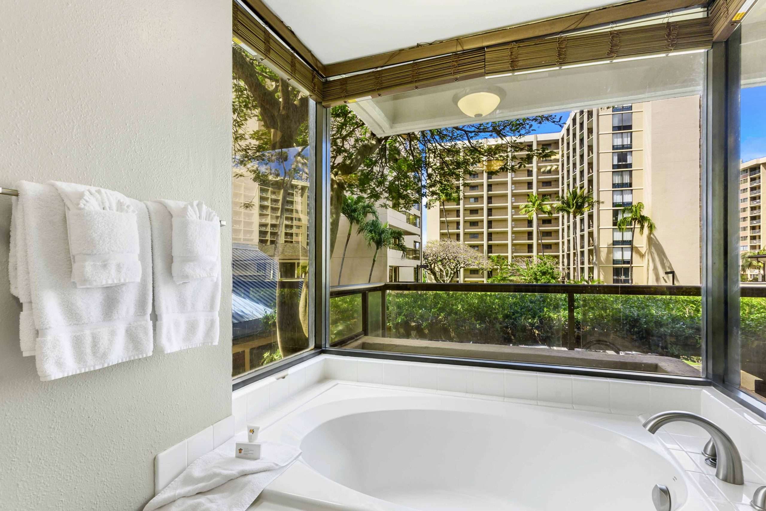 Soaking tub set in a corner window nook overlooking resort gardens and buildings.