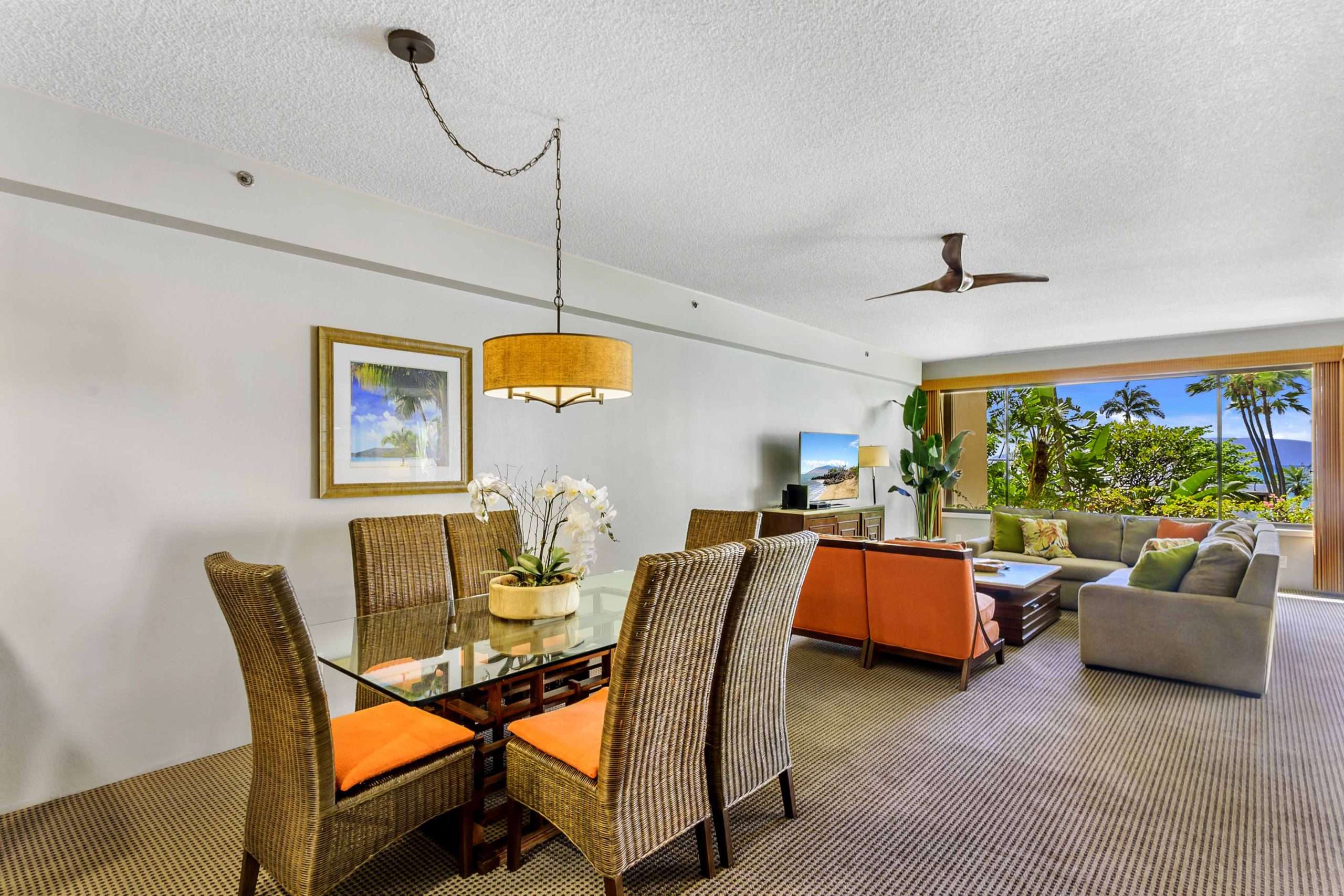 Open-plan suite with dining table, sofa, and large windows framing tropical gardens and the sea.