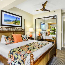 King bed with tropical linens, mirrored closet doors, and a ceiling fan in a Maui hotel one-bedroom suite.
