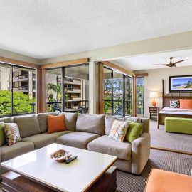 Spacious three-bedroom family suite in a Maui hotel featuring a living area with sectional sofa, adjacent king bedroom, and garden-view balcony.
