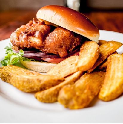 Crispy fish sandwich on a bun with lettuce and tomato alongside seasoned potato wedges at Captain Jack’s Island Grill in Maui.