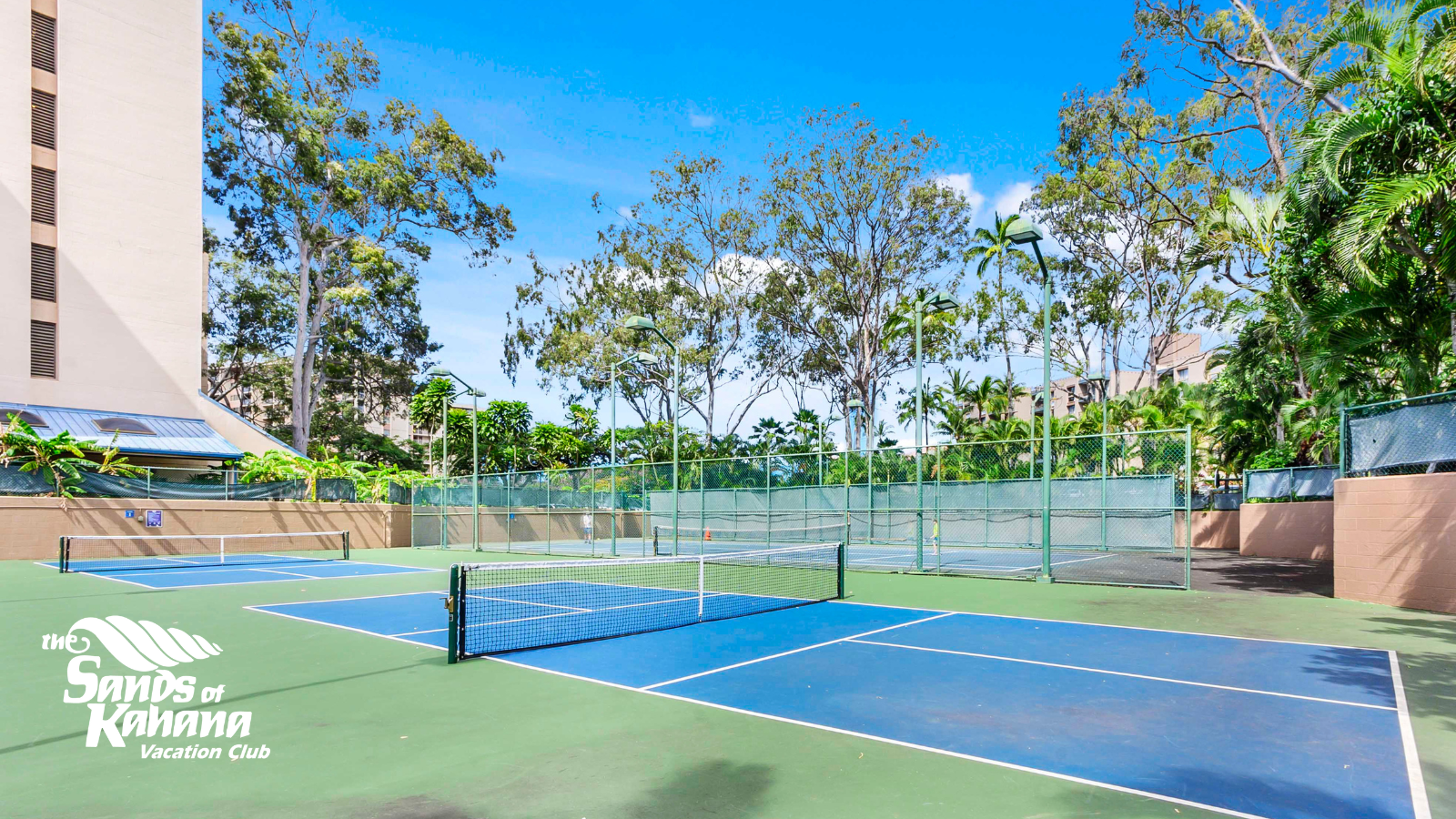 Outdoor tennis courts among lush greenery at Sands of Kahana amenities, with blue courts and nets against a resort backdrop.