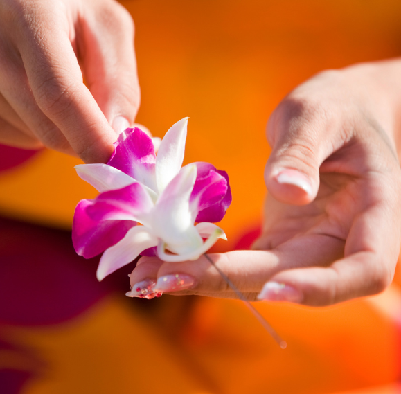 Detail shot of colorful orchid flowers being woven into a fresh lei on a sunny outdoor workshop table