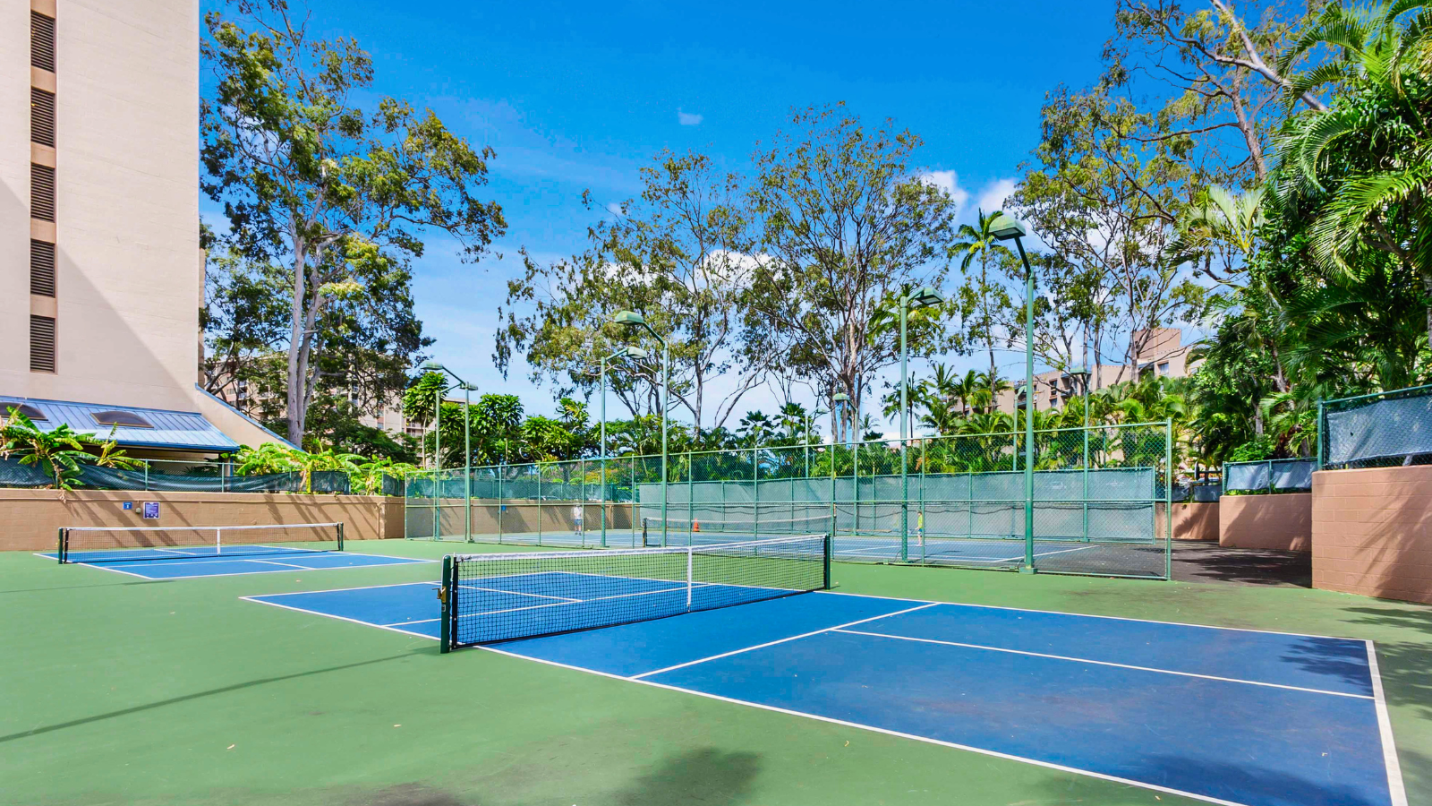 Outdoor tennis courts among lush greenery at Sands of Kahana amenities, with blue courts and nets against a resort backdrop.