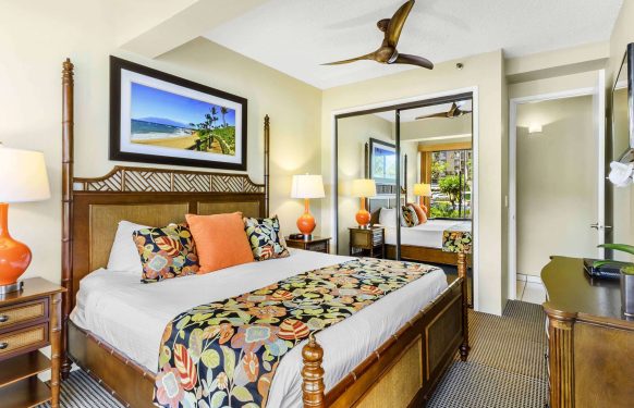 King bed with tropical linens, mirrored closet doors, and a ceiling fan in a Maui hotel one-bedroom suite.