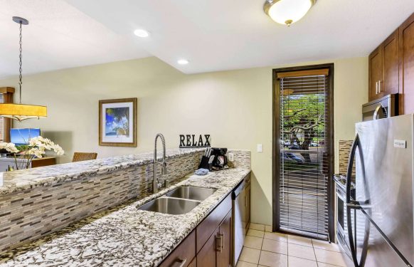 Maui hotel one-bedroom suite kitchenette with wood cabinets, stainless fridge, and a breakfast bar.