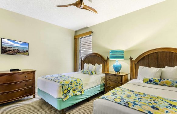 Two queen beds with floral runners, bedside table and lamp, and wood dresser in a Maui two-bedroom suite.